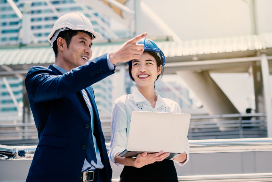 engineer with helmet pointing into distance as intern engineer smiles with a clipboard
